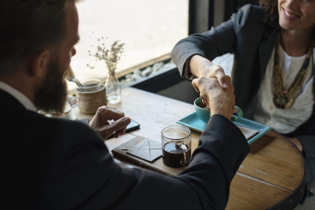 Two business partners shaking hands across a table during a working meeting