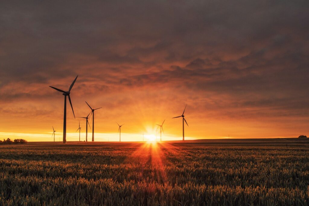 Row of wind turbines generating renewable energy in farmland at sunset